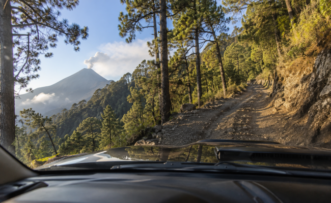 Vue depuis l'intérieur d'un 4x4 montant la route de l'Acatenango via la Finca San Sebastián, avec le volcan de Fuego en éruption en arrière-plan — Cyman Travel