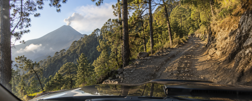 View from inside a 4x4 truck climbing the Acatenango route via Finca San Sebastián, Volcán de Fuego erupting in the background — Cyman Travel