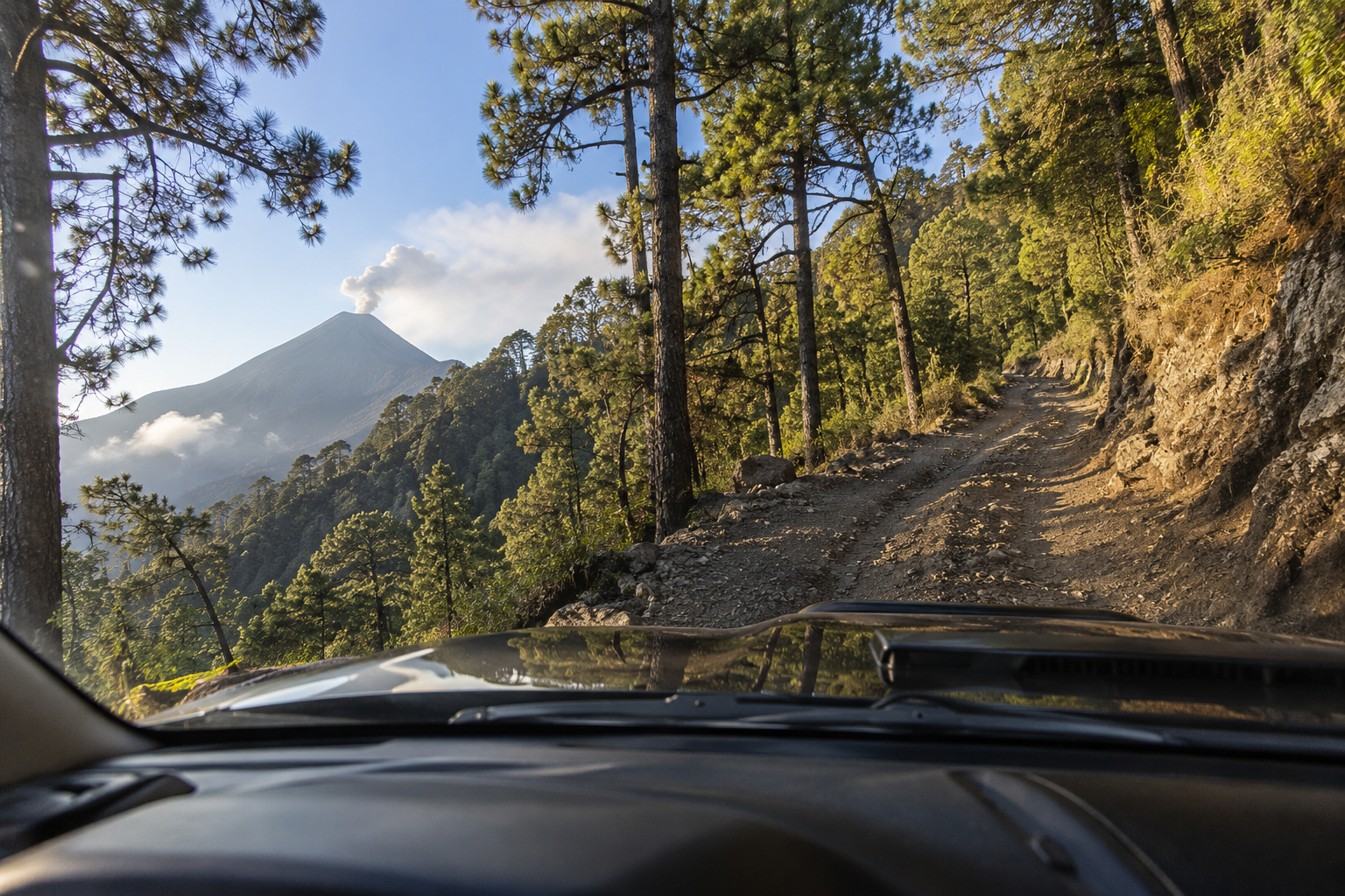 Vue depuis l'intérieur d'un 4x4 montant la route de l'Acatenango via la Finca San Sebastián, avec le volcan de Fuego en éruption en arrière-plan — Cyman Travel
