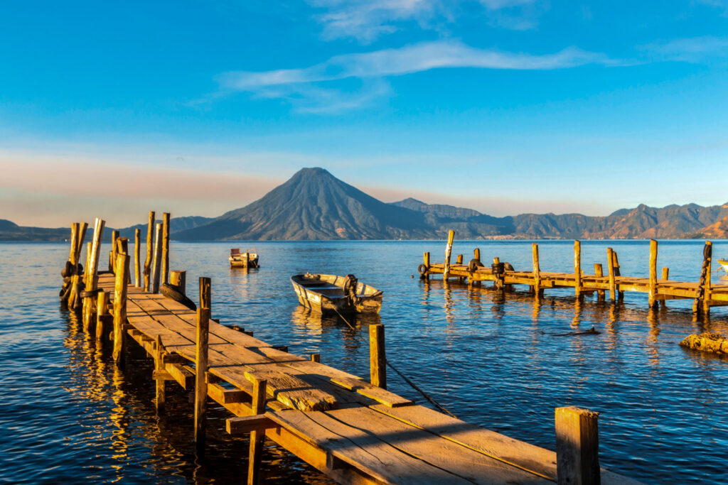 Lake Atitlán Guatemala surrounded by three volcanoes with colorful wooden boat in foreground — day trip from Antigua